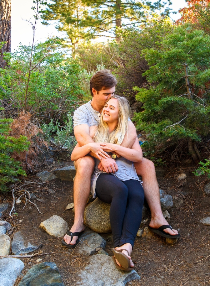 photo of couple cuddling on a rock surrounded by trees