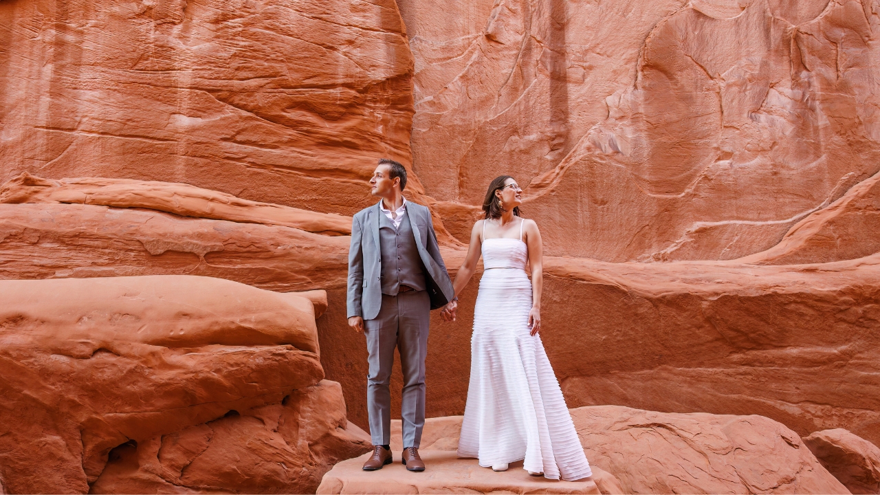 photo of bride and groom standing on a rock, holding hands and looking in opposite directions