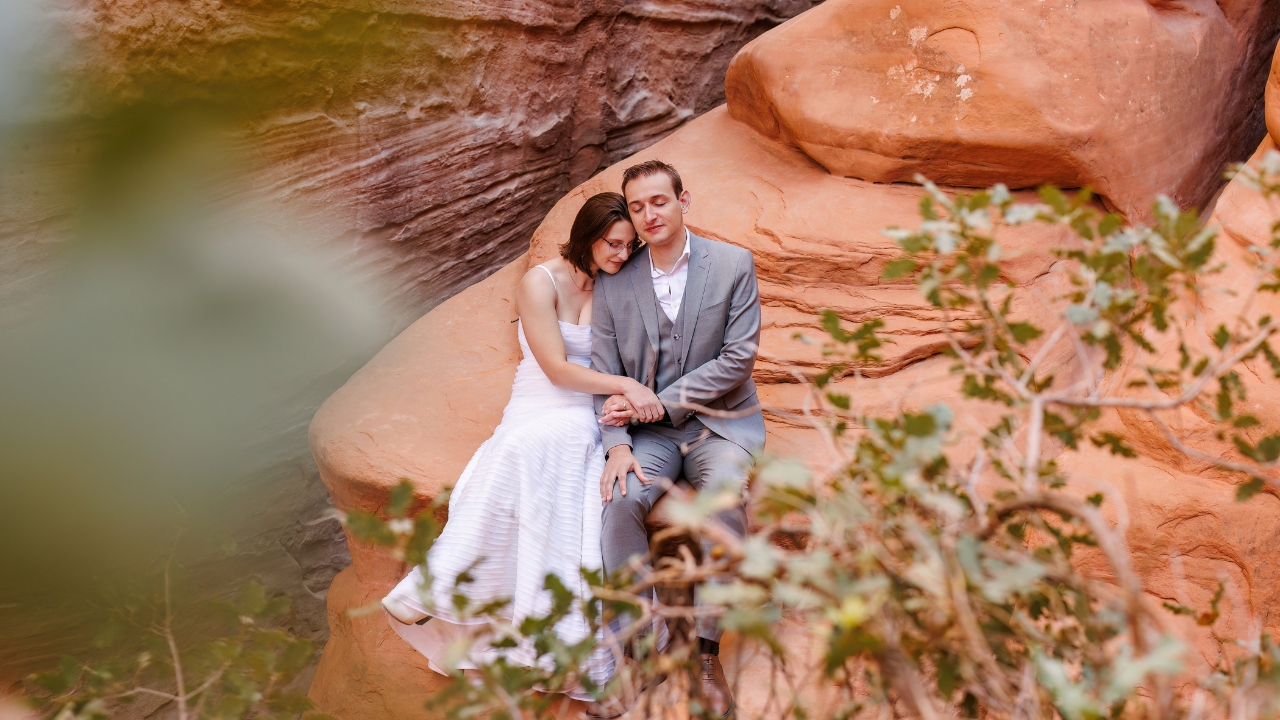 photo of bride and groom sitting on a rock holding hands and embracing 