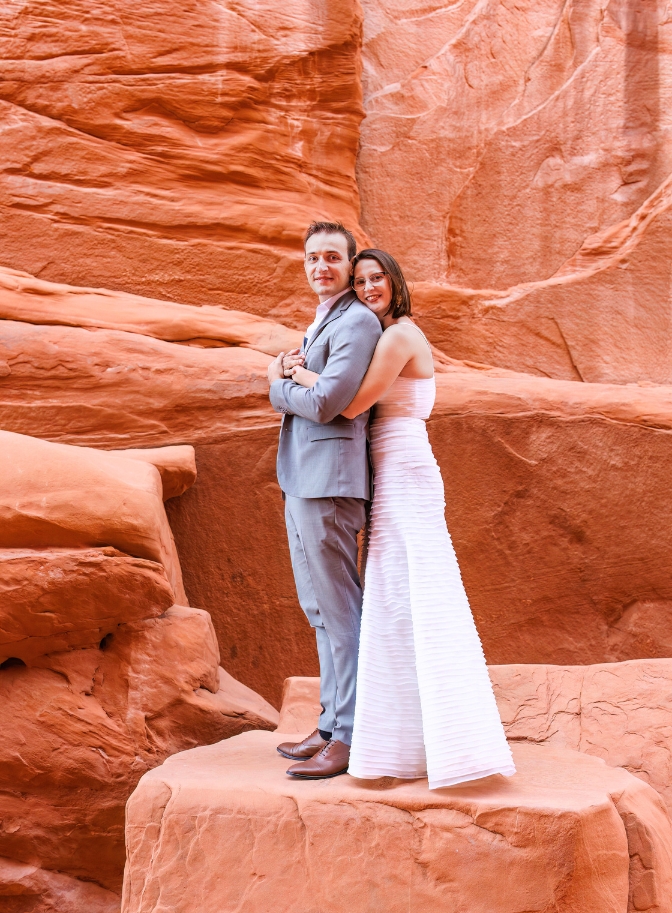 photo of bride holding groom from behind and standing on a rock at Arches National Park