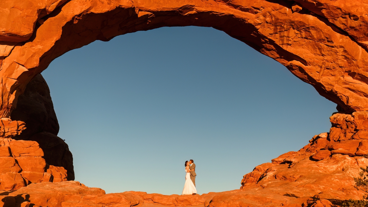 photo of bride and groom kissing in the eye of an arch at sunset