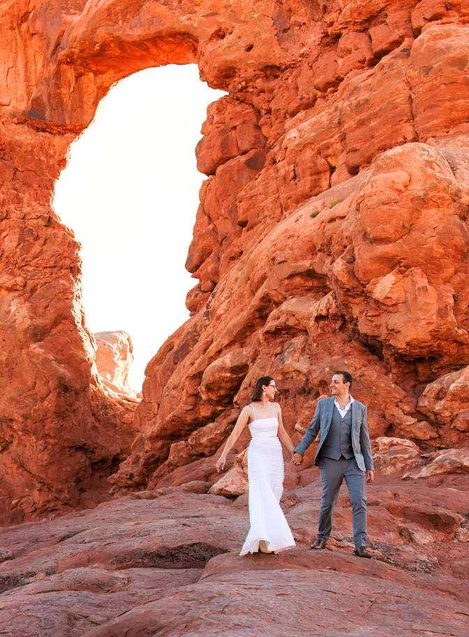 photo of bride holding hands and walking with arch behind them