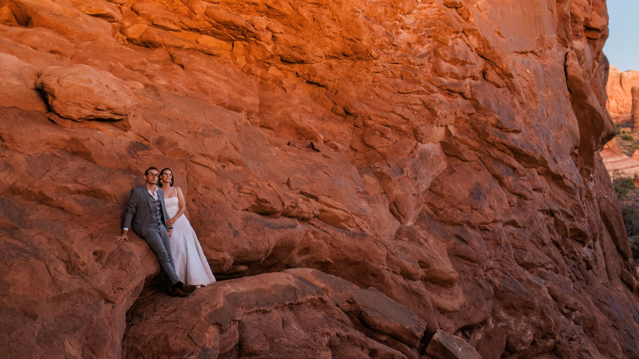 photo of bride and groom standing along edge of rock wall watching sunset