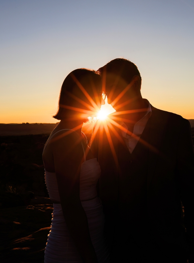 photo of bride and groom with foreheads touching and sun setting between them