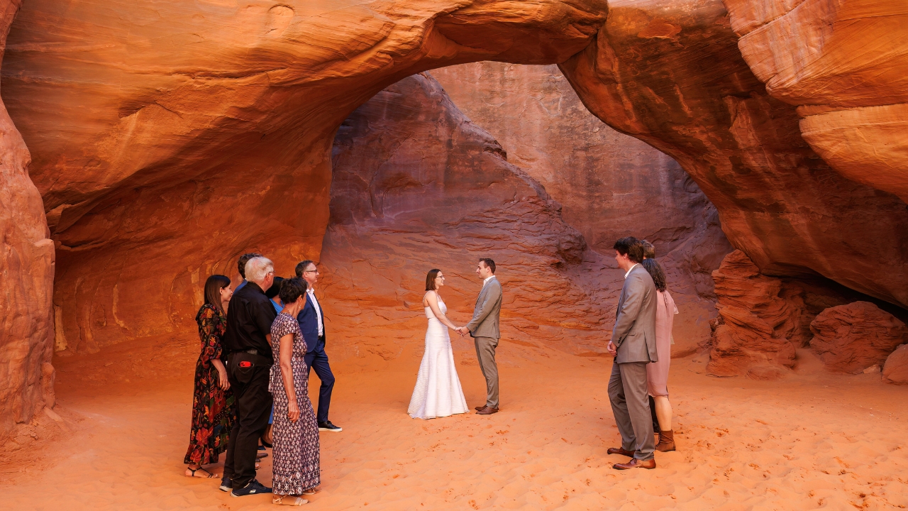 photo of bride and groom holding hands with family surrounding them under arch in Utah