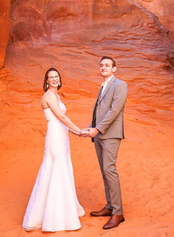 bride and groom holding hands and smiling as they look off in the distance