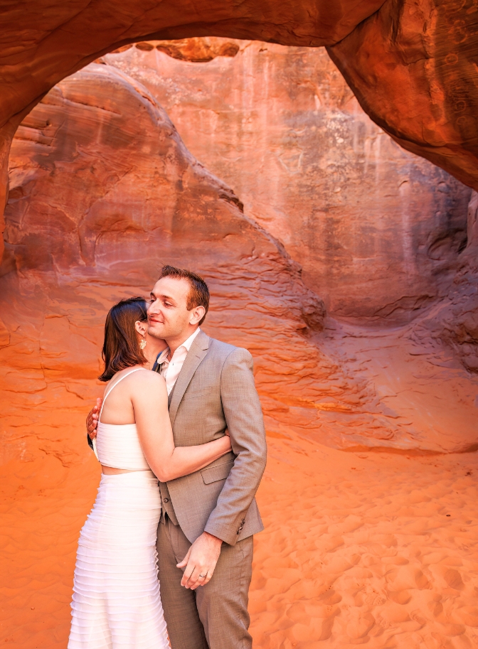 Photo of bride and groom embracing with red rock surrounding them.