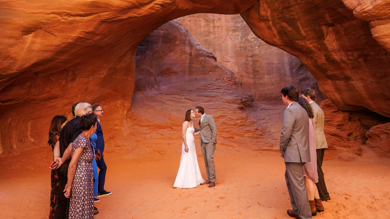 photo of bride and groom kiss under arch with family and friends surrounding them for their National Park elopement