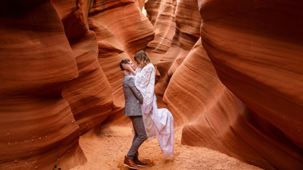 photo of groom lifting bride up in the air as she holds his face in slot canyon for elopement