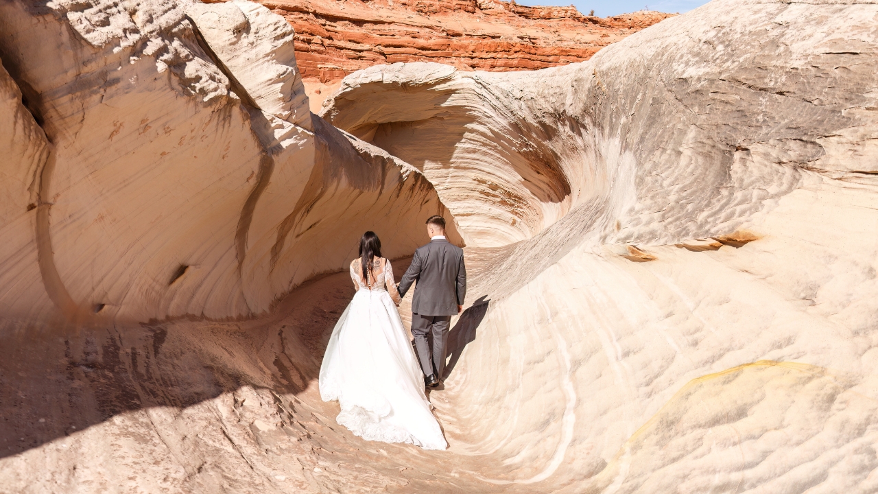 photo of bride and groom holding hands walking into white and tan slot canyon