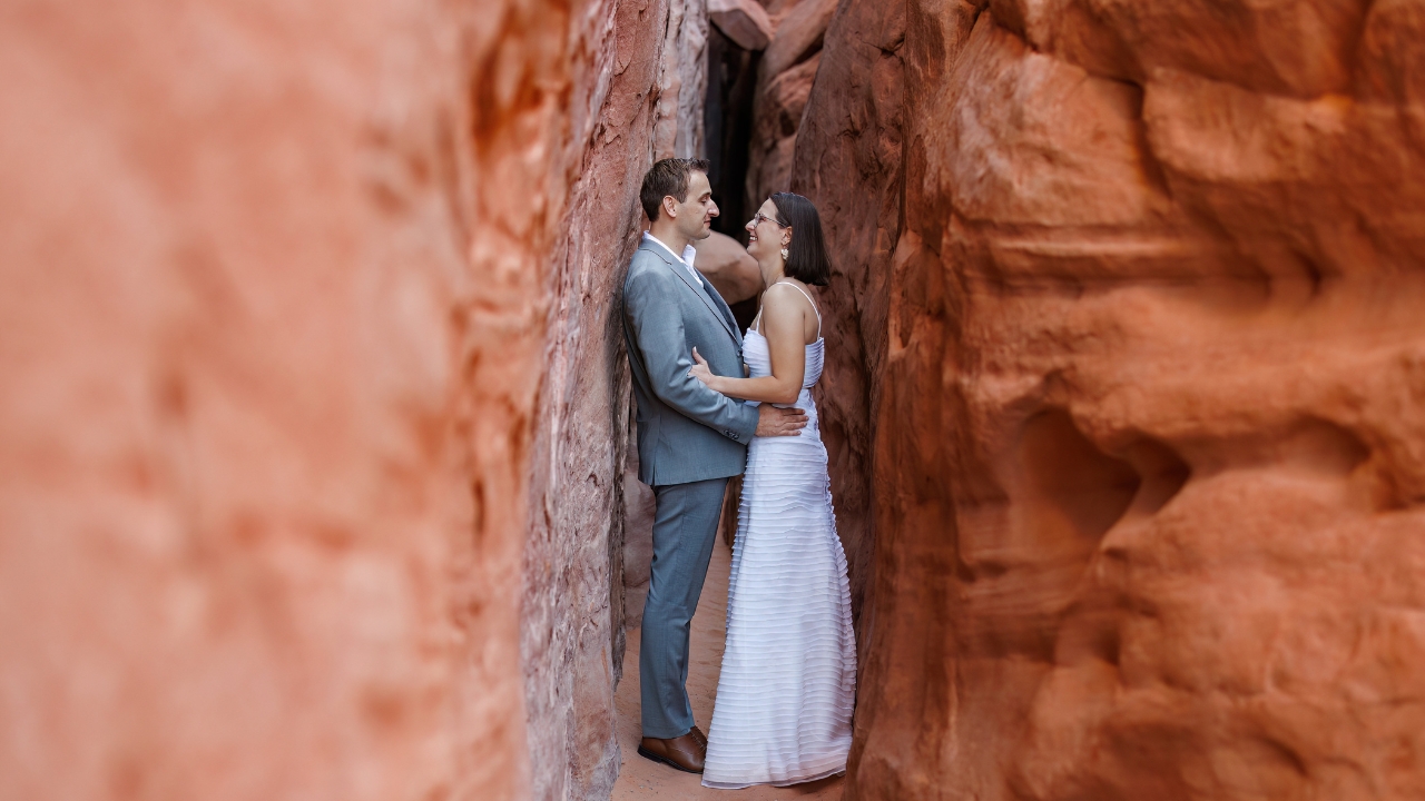 photo of bride and groom holding each other and laughing in between a slot canyon at Arches National Park