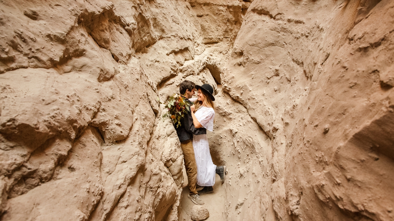 photo of bride and groom holding each other and smiling while leaning against a tan slot canyon