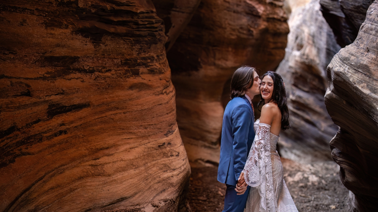 photo of groom kissing bride on the cheek inside of a slot canyon at Zion National Park