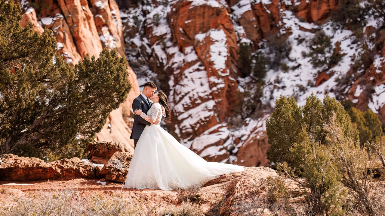 photo of bride and groom kissing on wedding day with snow covered red rocks behind them