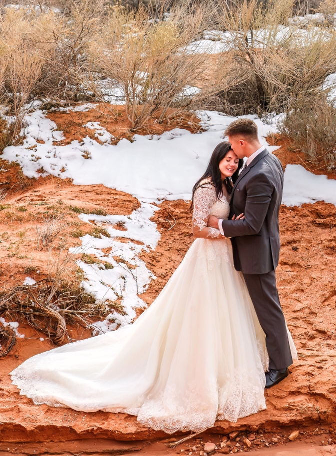 photo of groom kissing bride on the forehead with snow covered red rock surrounding them