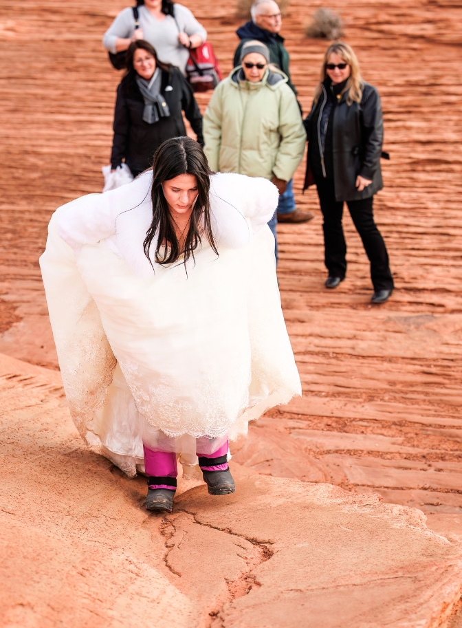 photo of bride hiking in snow boots with wedding guests behind her