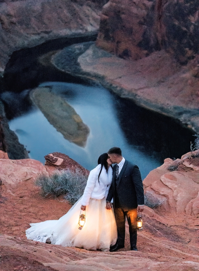 photo of bride and groom kissing while holding lanterns with the Colorado River behind them.