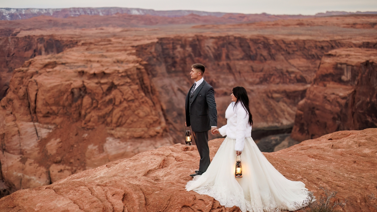 photo of bride and groom holding lanterns in their hands as they look on with a canyon behind them