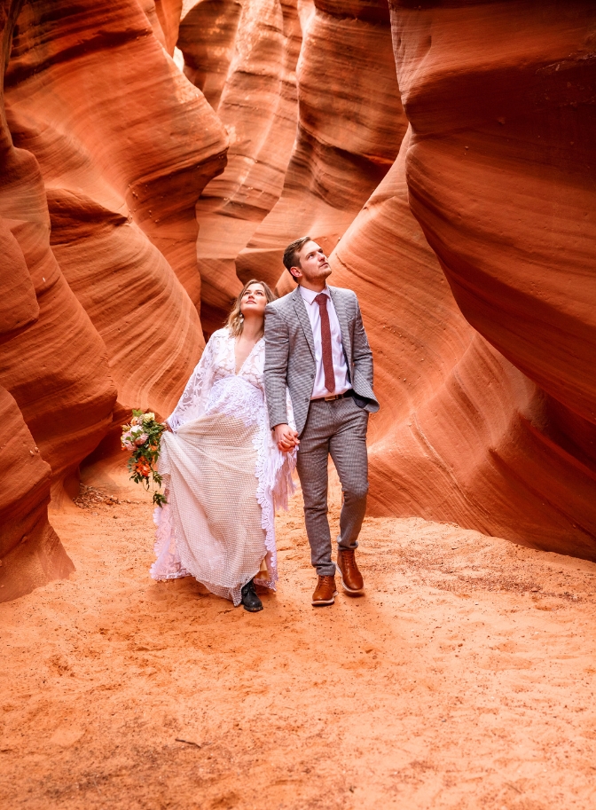 photo of bride and groom holding hands and looking up around at Waterholes Canyon