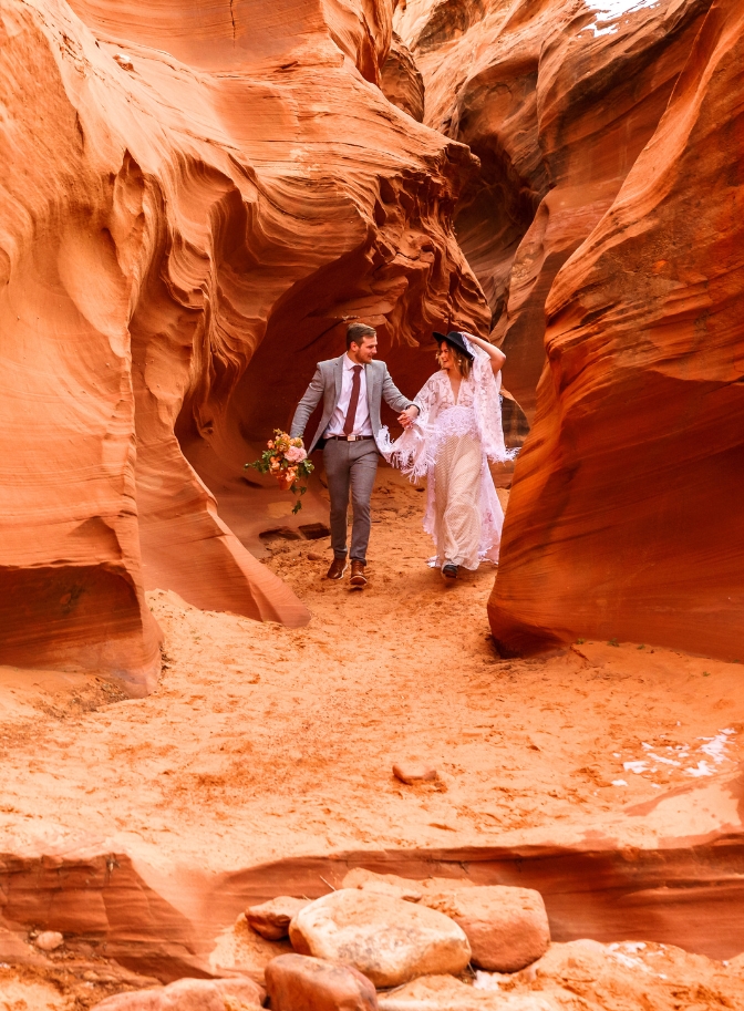 photo of bride and groom walking hand in hand between red rock slot canyon