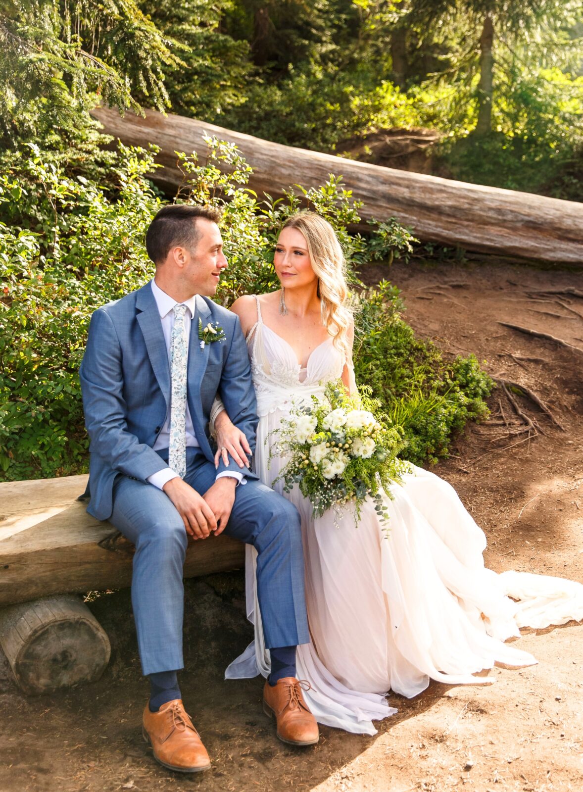 photo of bride and groom sitting on a wooden bench on a trail and staring into each others eyes for Mt Rainier elopement