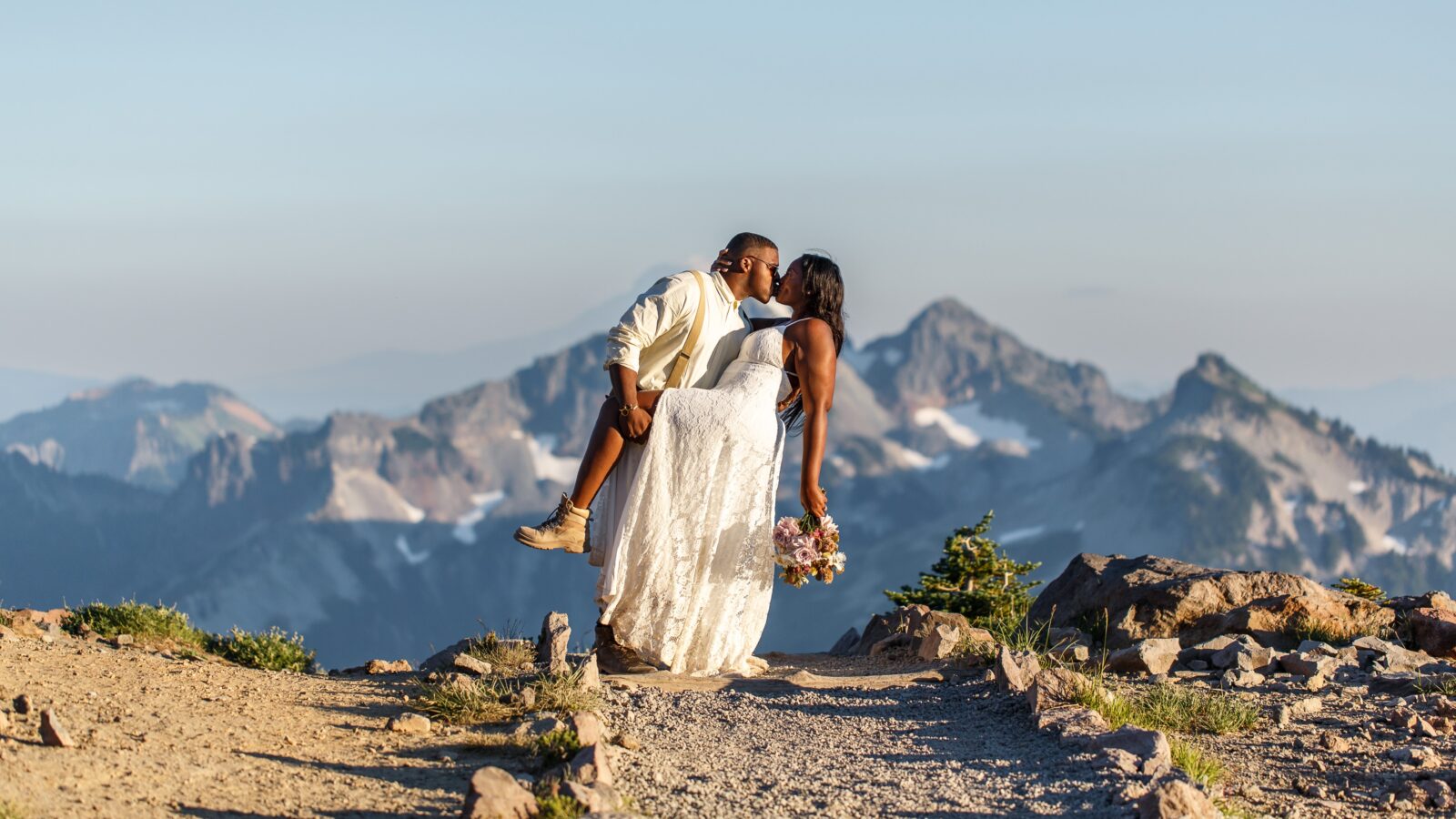 photo of groom holding up brides leg while they kiss with a mountain range behind them