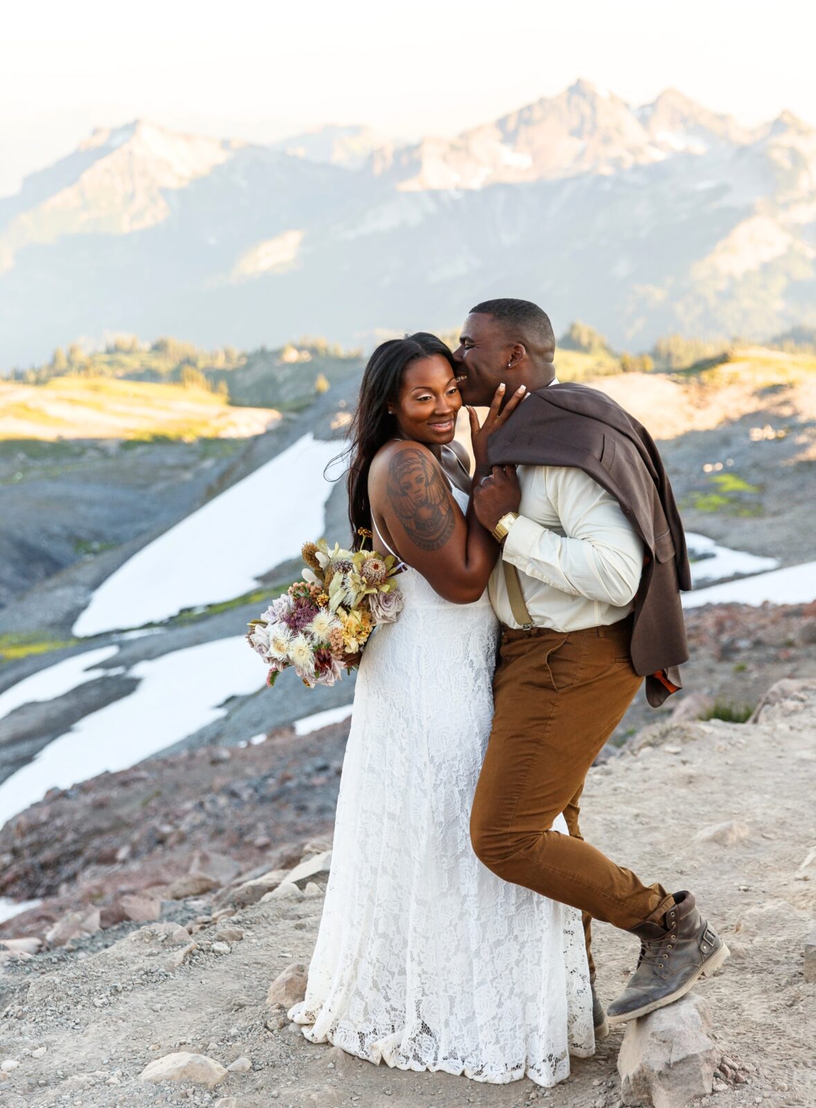 photo of groom and bride embracing while groom kisses her cheek with mountains behind them