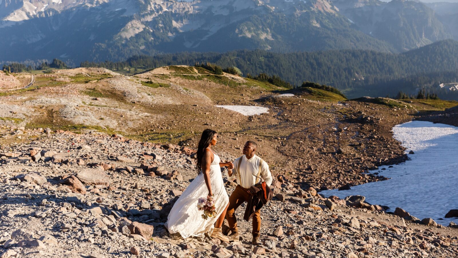 photo of groom guiding bride down rocky terrain on wedding day