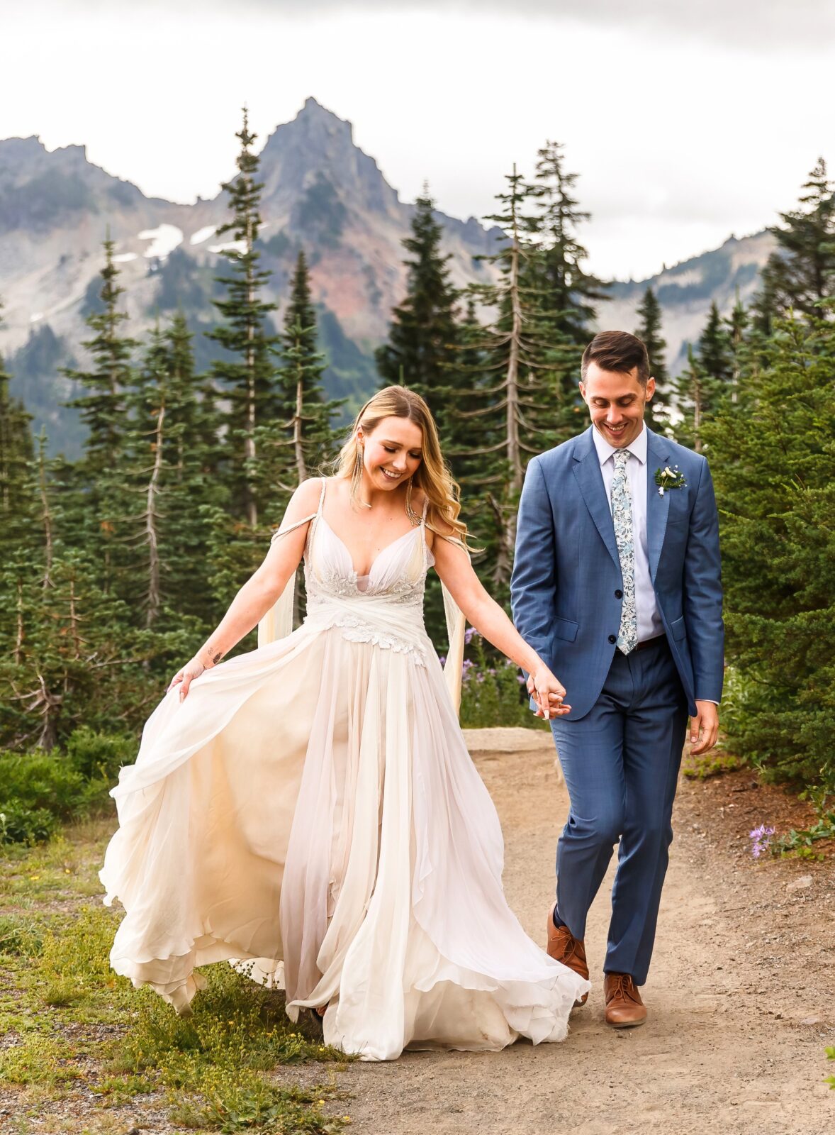 photo of bride and groom walking along a trail, holding hands, and smiling at their Mount Rainier elopement