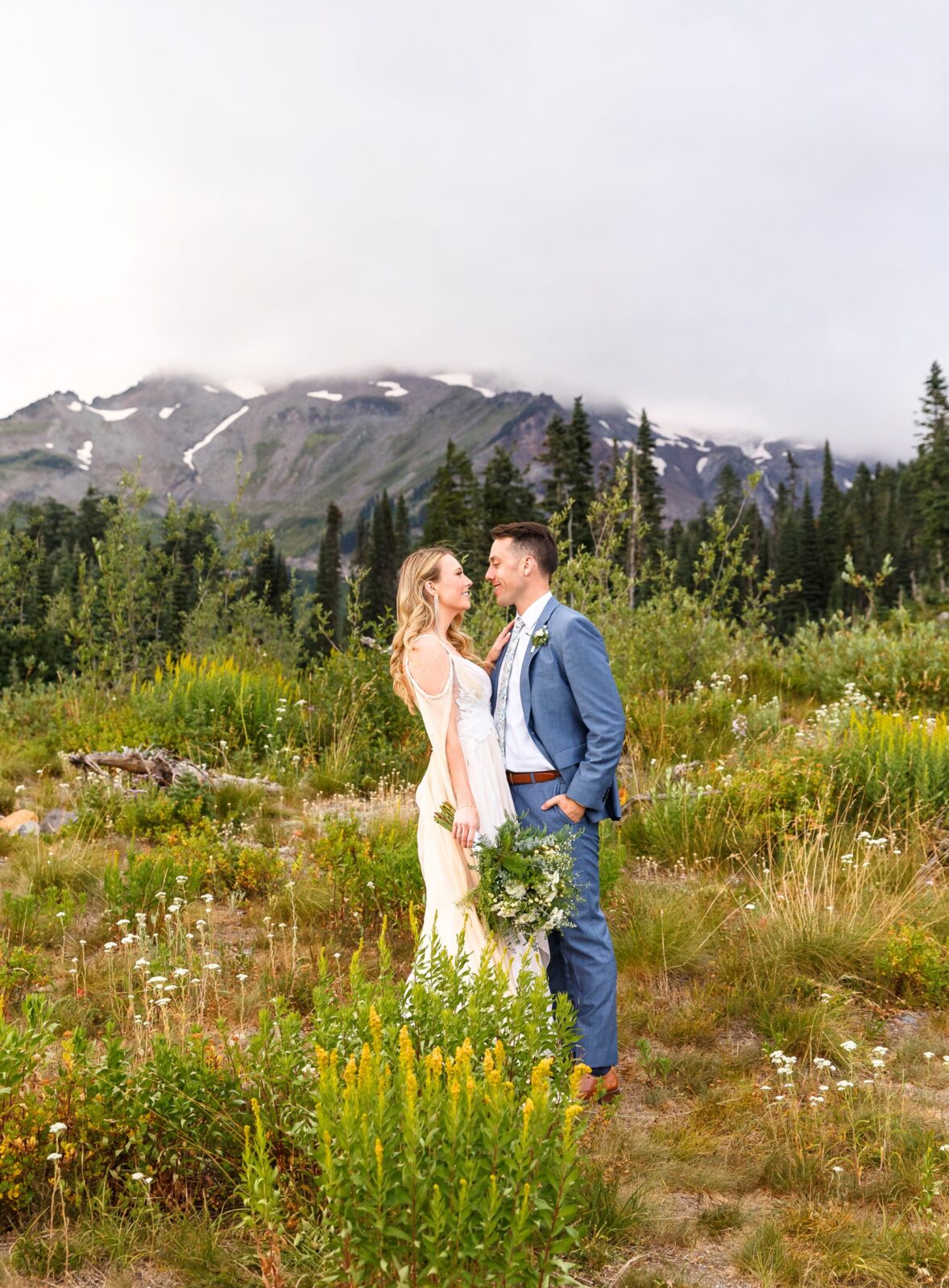 photo of bride and groom staring at each other lovingly while surrounded by wildflowers and a mountain range behind them