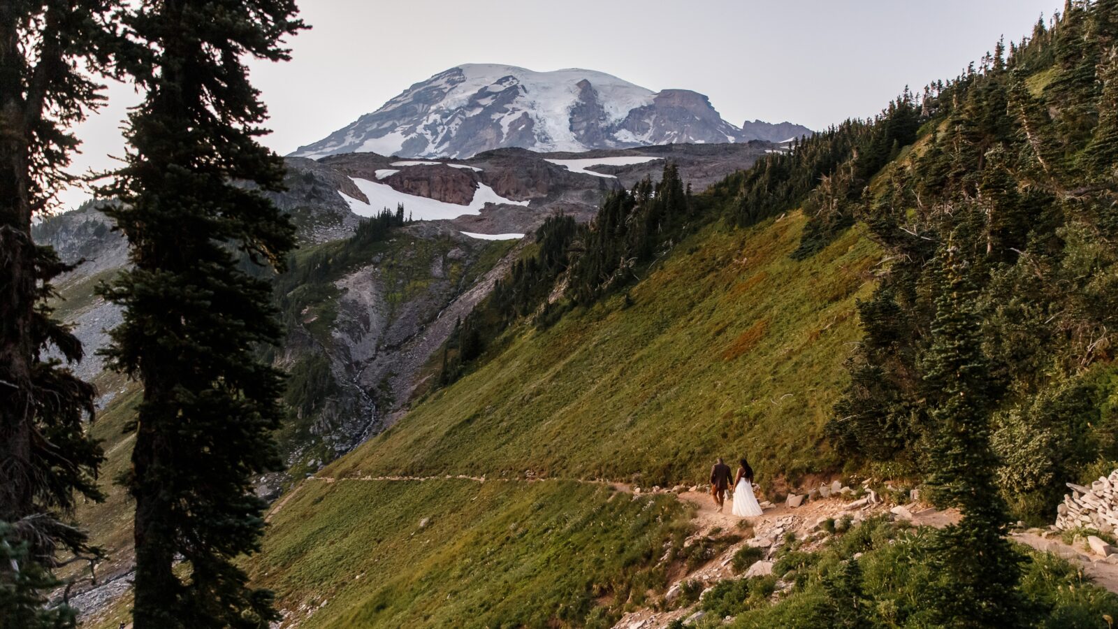 photo of bride and groom walking along trail with views of Mount Rainier in the distance