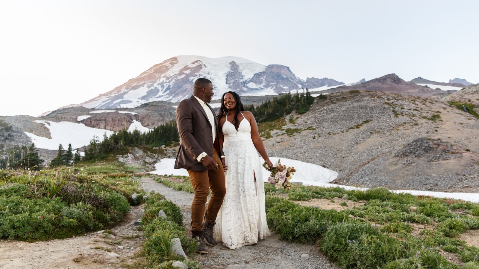 photo of couple holding hands and laughing on wedding day with mountain behind them at Mt Rainier elopement