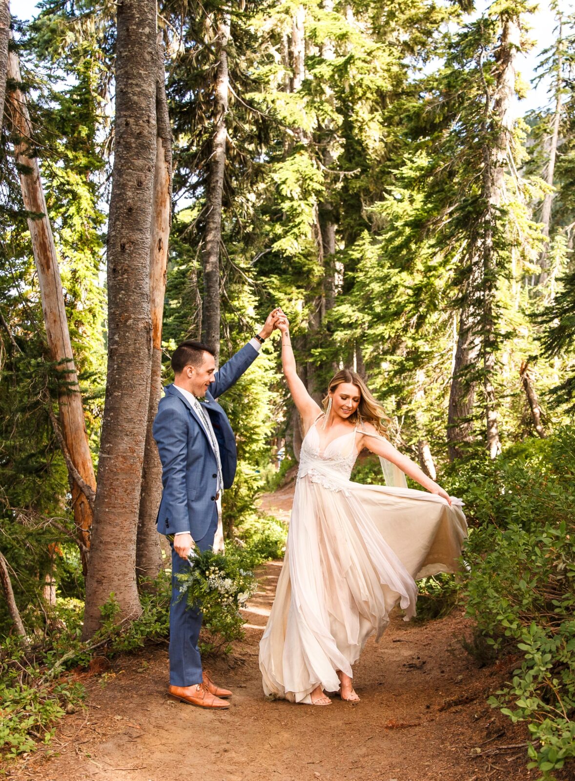 photo of groom spinning bride in wedding gown on trail surrounded by trees