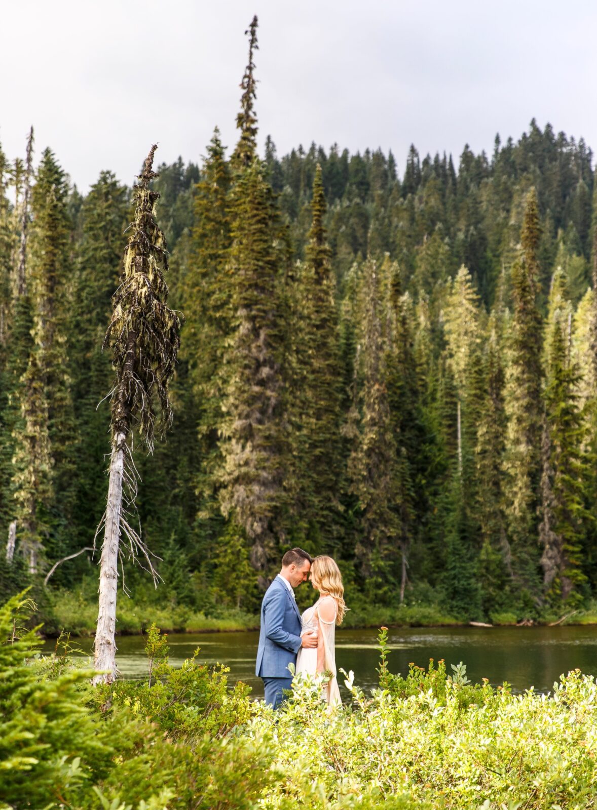 photo of bride and groom touching foreheads with lake and trees surrounding them