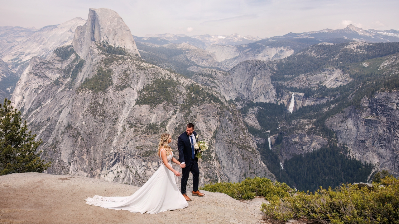 photo of bride and groom holding hands with view of Yosemite valley behind them