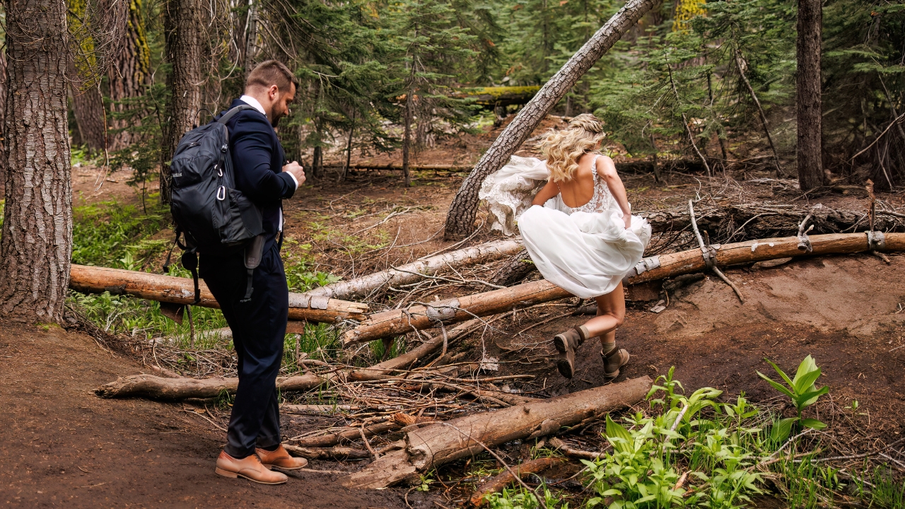 photo of bride jumping over fallen logs on wedding day as groom follows behind