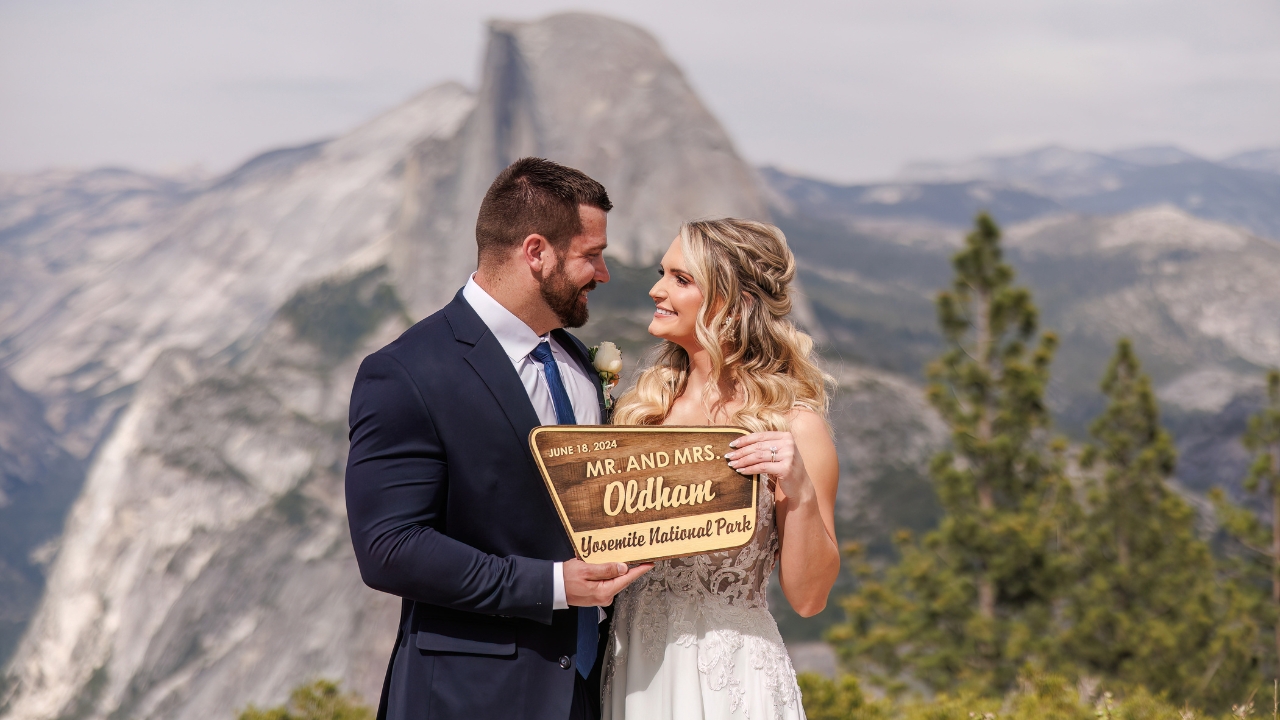 photo of bride and groom standing at Glacier Point holding wedding sign