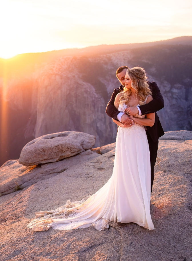 photo of bride and groom embracing and groom kissing her on the cheek with sunset behind them