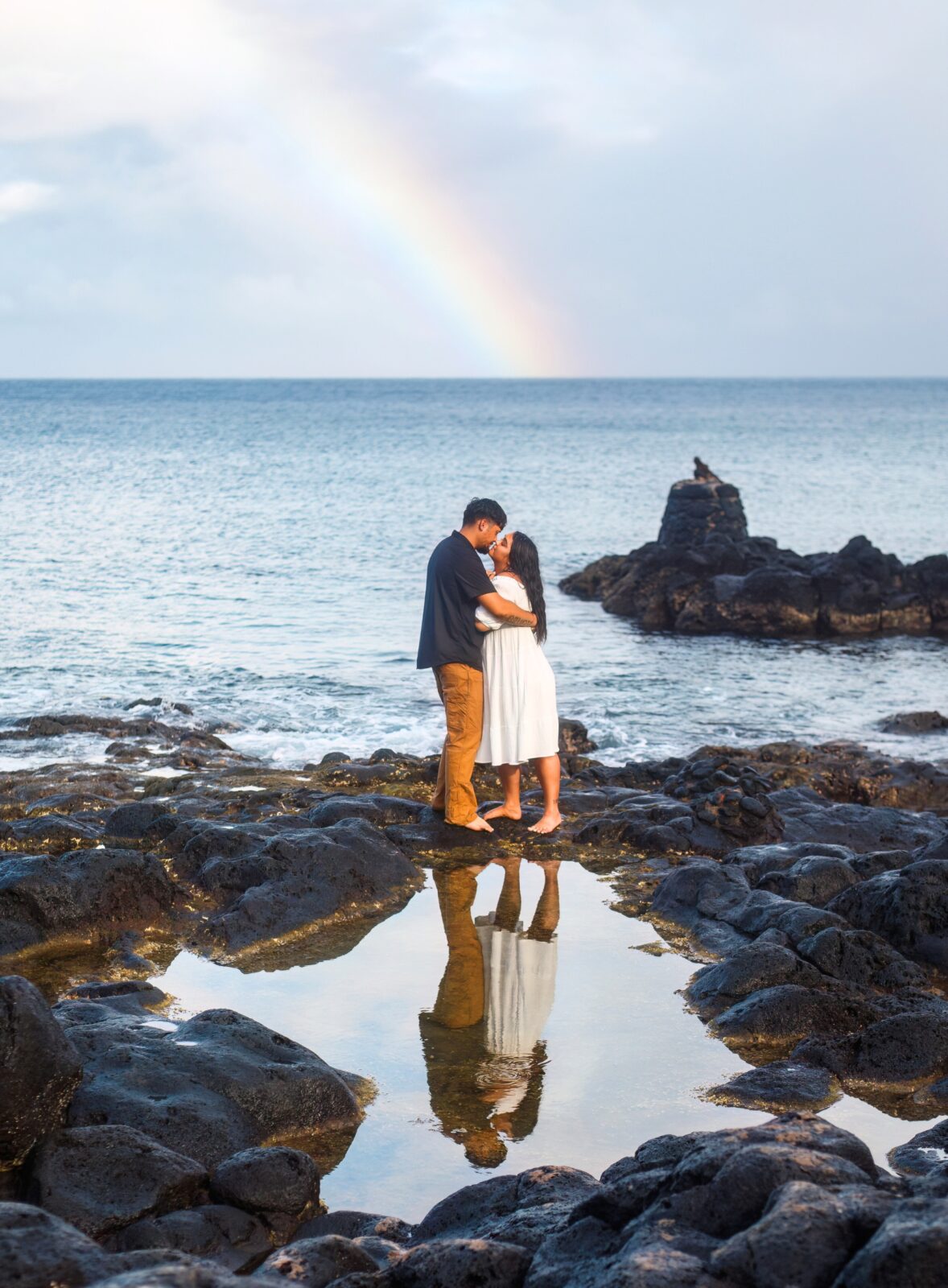 photo of couple kissing with rainbow behind them and reflection in water