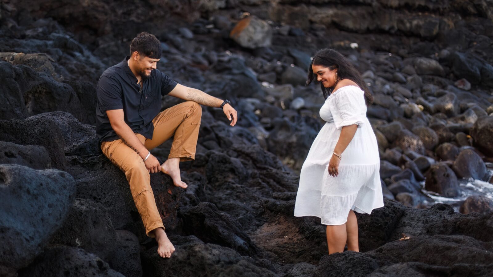 photo of couple climbing over lava rocks for a Hawaii engagement session and laughing