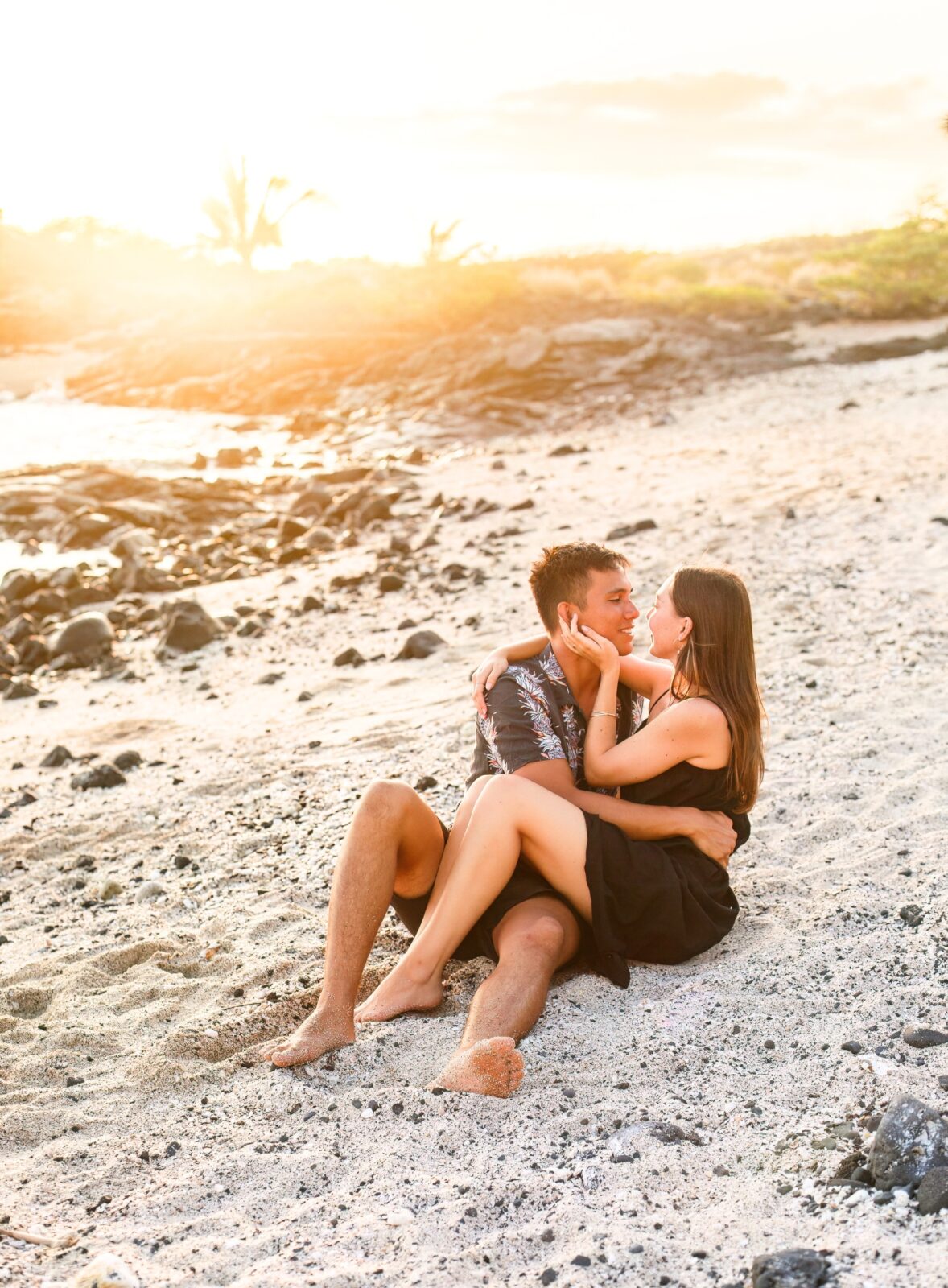 photo of couple sitting on beach in Hawaii as they hold each other and look into each other's eyes