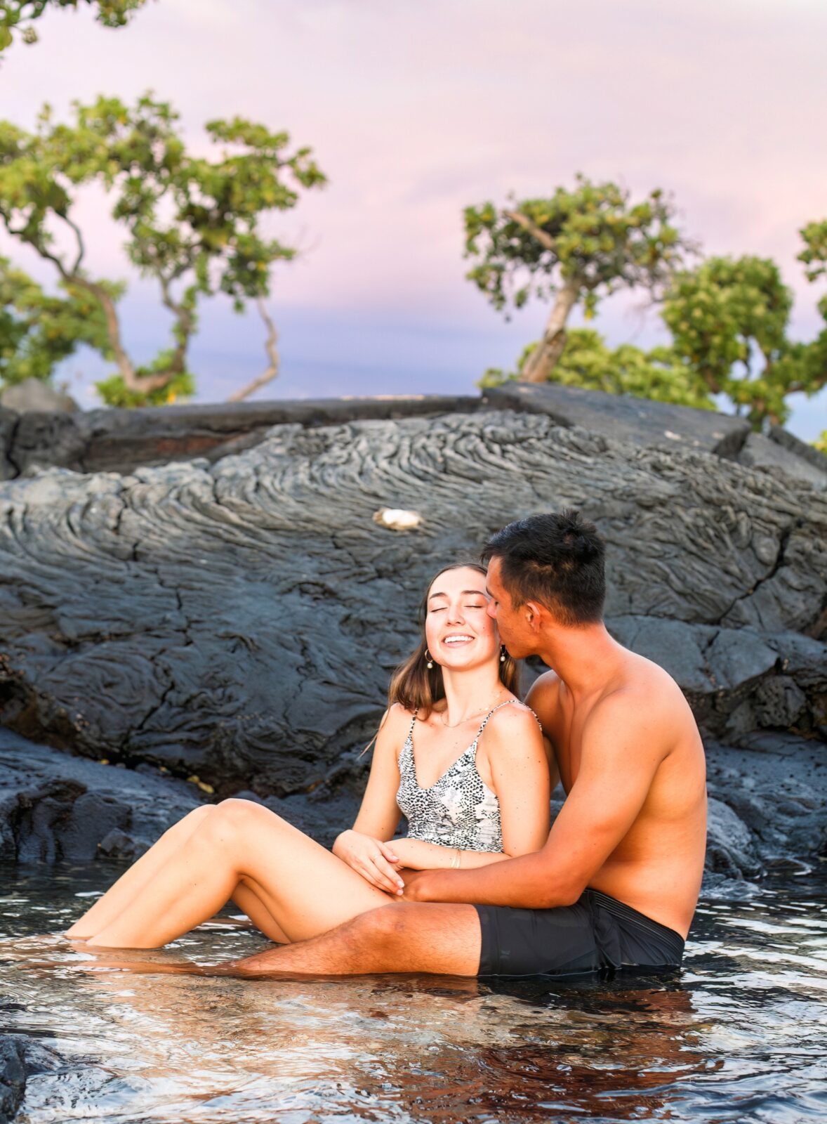 photo of couple embracing in the water and he kisses her on the cheek while she smiles