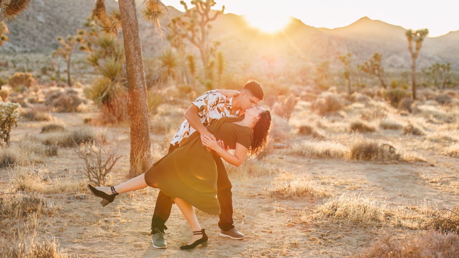 photo of guy dipping his fiancée and kissing her with the sun setting behind them 