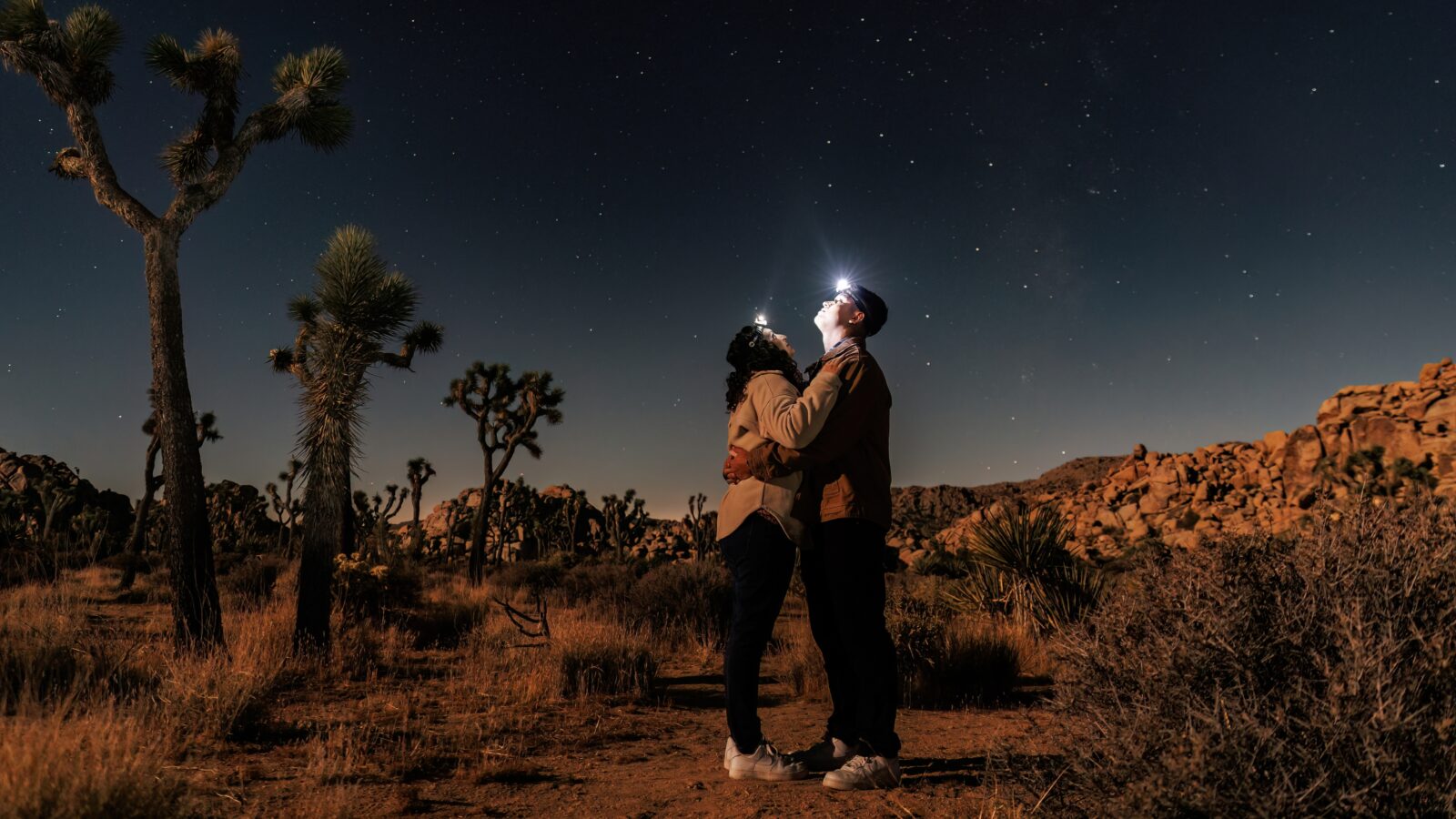 photo of couple holding each other and staring up at the sky with headlamps on to looking at the stars