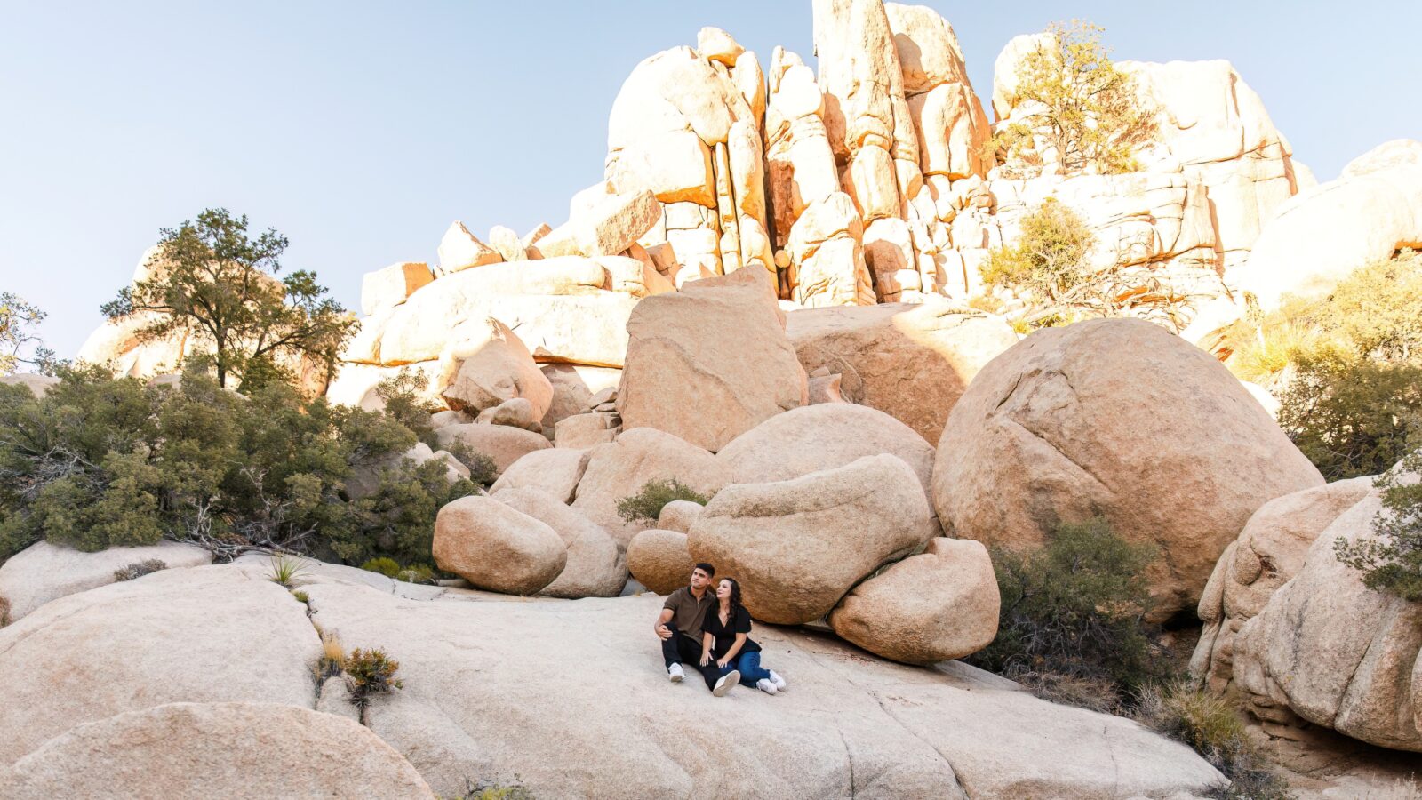 photo of couple sitting down on rock face and staring off in the distance with large rocks behind them