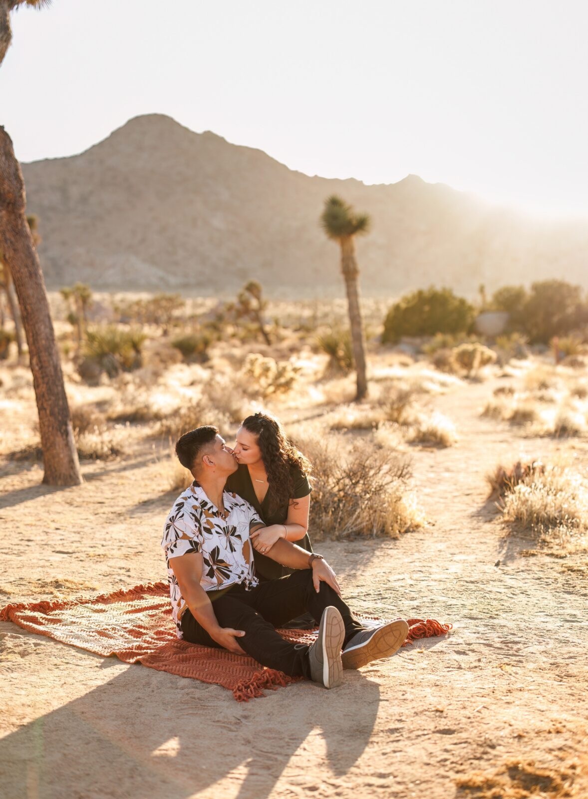 photo of couple kissing on an orange blanket in the desert for their Joshua Tree engagement photoshoot