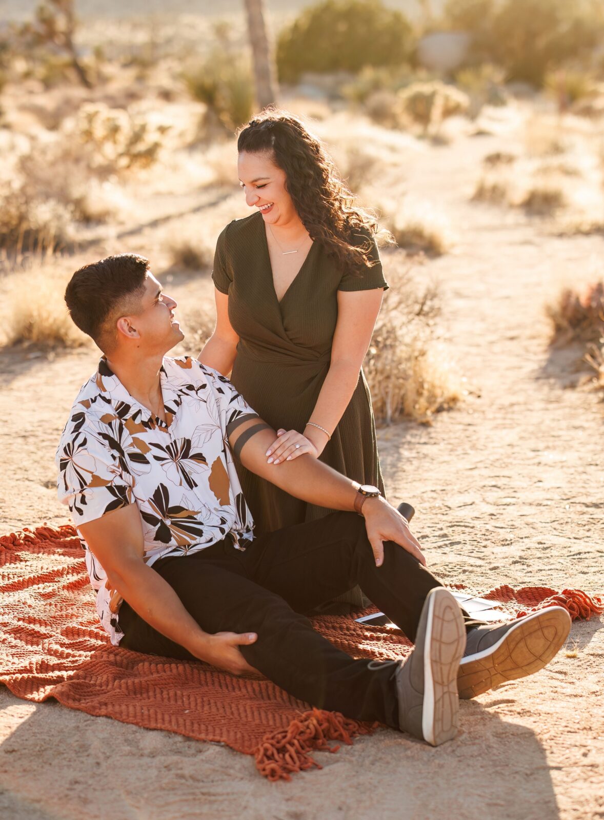 photo of woman kneeling beside her fiancée and holding his arm as they laugh