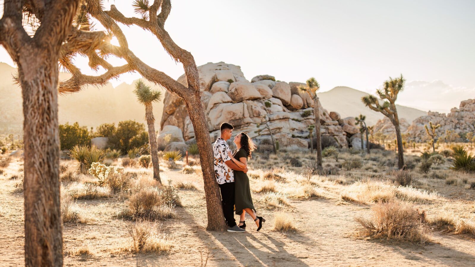 photo of couple leaning against a tree and looking into each other's eyes smiling in the desert