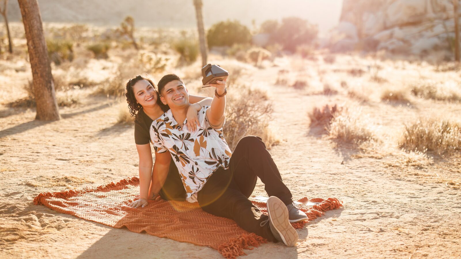 photo of couple sitting on blanket taking a selfie with a polaroid camera