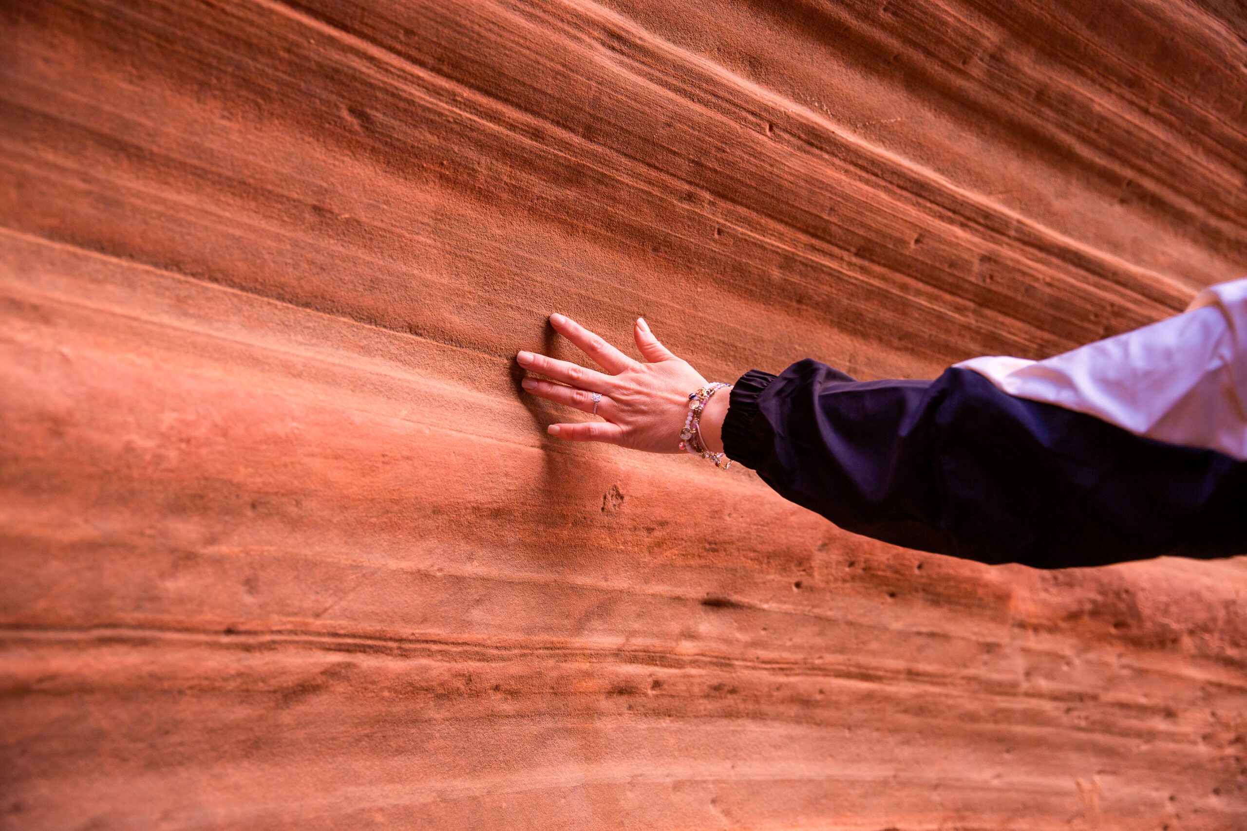 a woman running her hands on the red rocks during the couples surprise proposal adventure